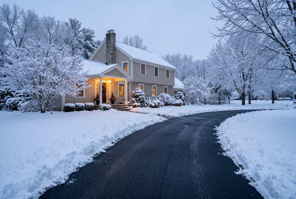 Cleanly plowed driveway lined with fresh snow banks in front of a warmly lit home